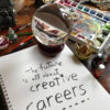 Photograph of a crystal ball and art supplies atop a notepad. On the notepad is writing which reads "The future is all about creative careers"
